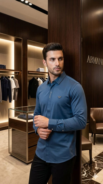 "Man wearing branded  steel blue long-sleeve polo shirt with EA eagle logo badge, inside a luxury Armani boutique"

