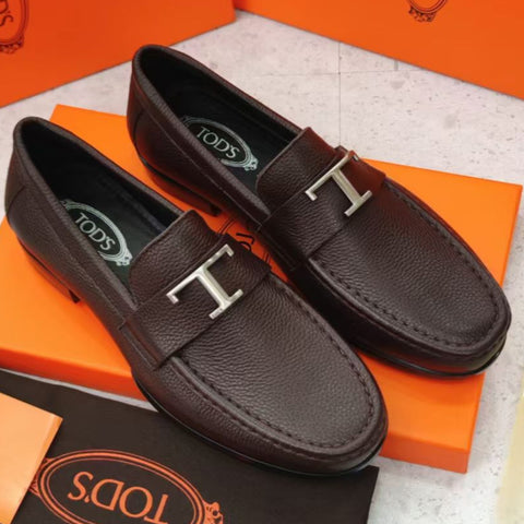 Pair of brown loafers with silver 'T' logo on orange and black Tods packaging.