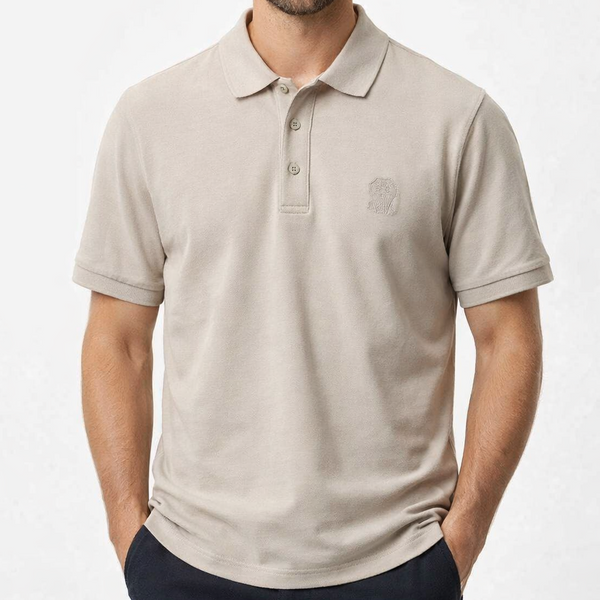 Man wearing a sand beige short-sleeve luxury piqué polo shirt with tonal crest embroidery and horn-effect buttons, inside an upscale boutique"