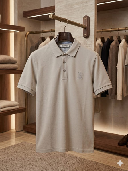 Man wearing a sand beige short-sleeve luxury piqué polo shirt with tonal crest embroidery and horn-effect buttons, inside an upscale boutique"