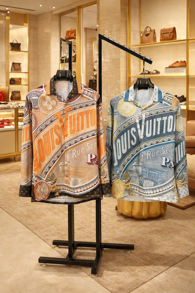 Premium brand men's long sleeve shirts in orange and blue colorways featuring 1 Rue Scribe Paris heritage graphic print with LV monogram pattern on display stands